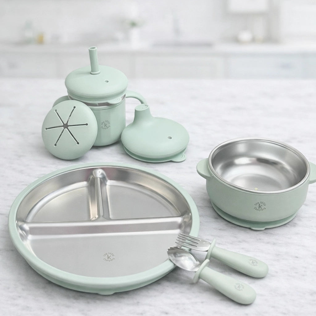 Set of light green children's tableware including a plate, bowl, cup, and cutlery on a marble surface.