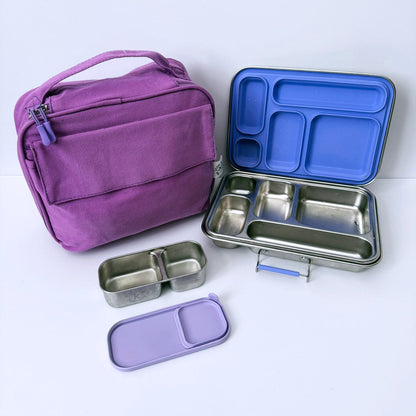A purple fabric lunch bag shown next to an open stainless steel bento lunch box with a blue lid insert, plus two small compartment containers and a purple lid, all arranged on a clean white background.