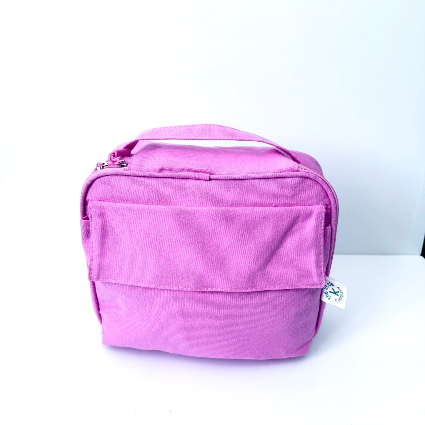 A pink GOTS certified organic cotton lunch bag with a top handle and front zippered pocket, photographed on a plain white background.