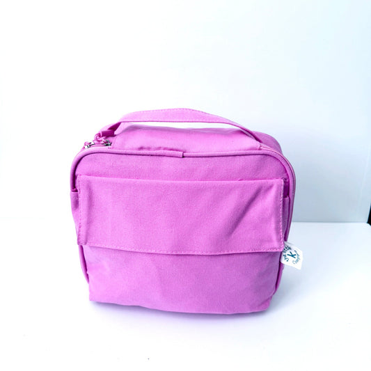 A pink GOTS certified organic cotton lunch bag with a top handle and front zippered pocket, photographed on a plain white background.